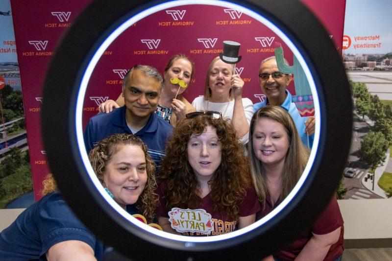 Seven employees photographed through a ring light against a Virginia Tech step-and-repeat